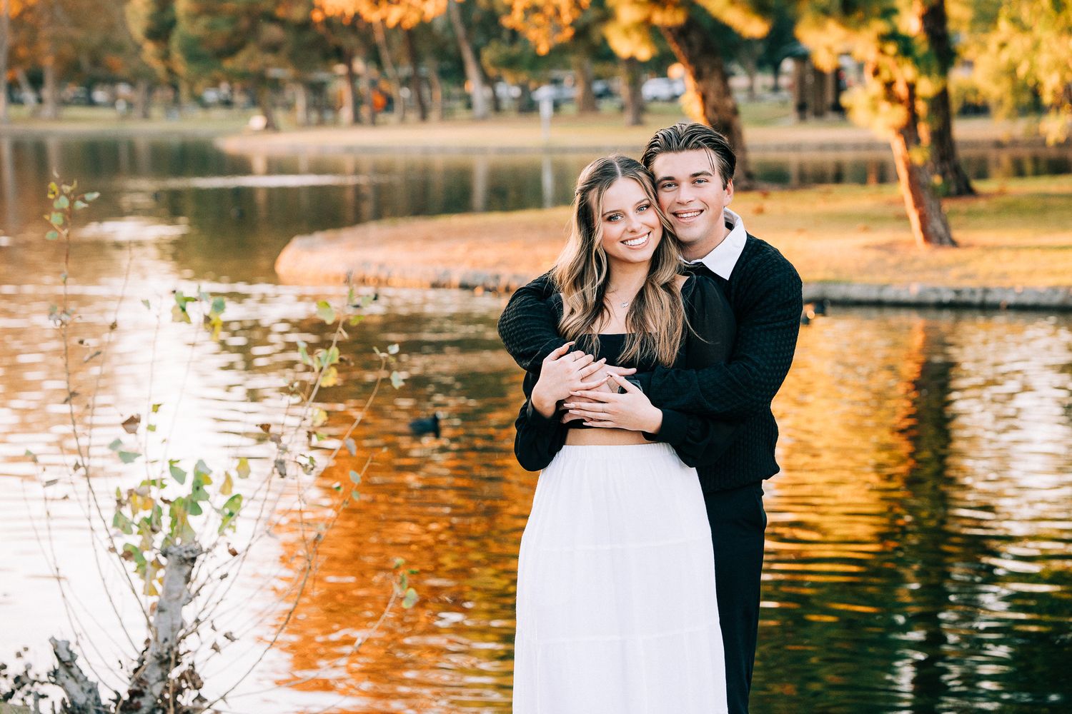Couple shares intimate moment by lakeside during golden hour autumn photoshoot.