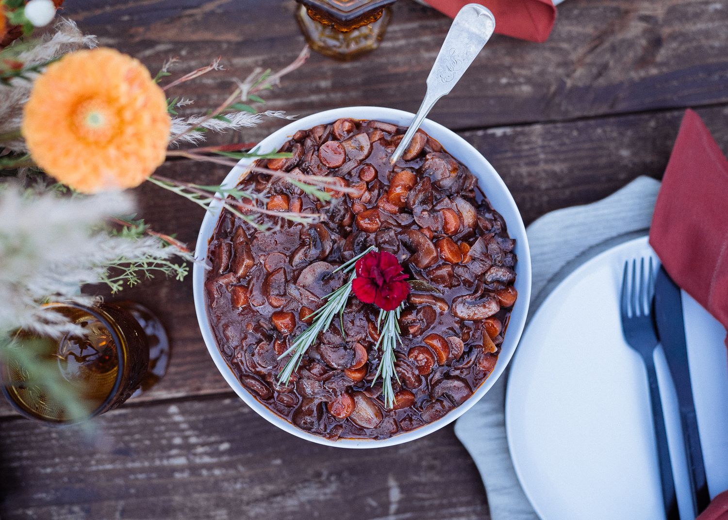 A bowl of dark chocolate dessert with a spoon and table settings on a rustic wooden surface.