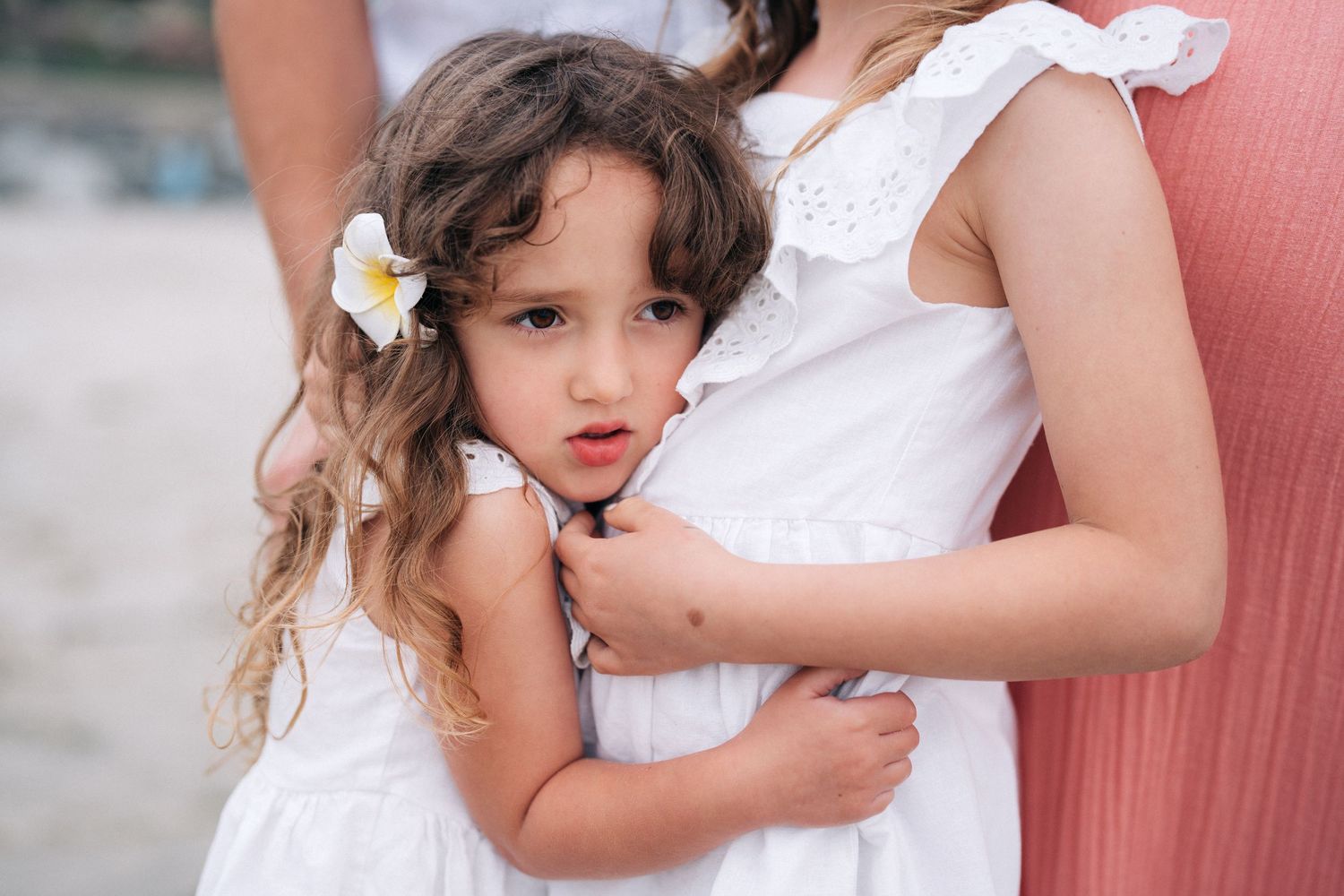 A close-up photograph of a person wearing a white lacey dress with pink accents and flower hair ornaments.
