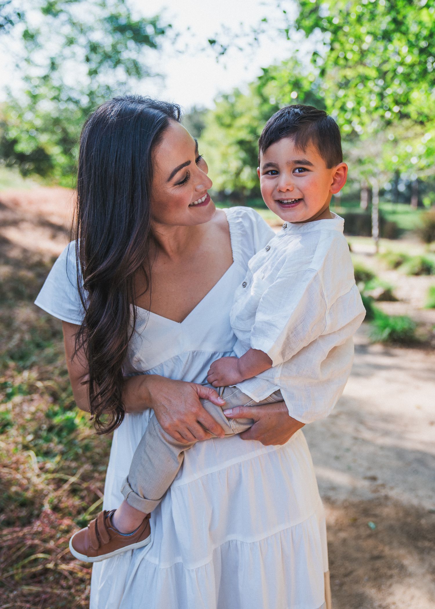 Mother and young child share a joyful moment together while wearing matching white outfits on an outdoor path.