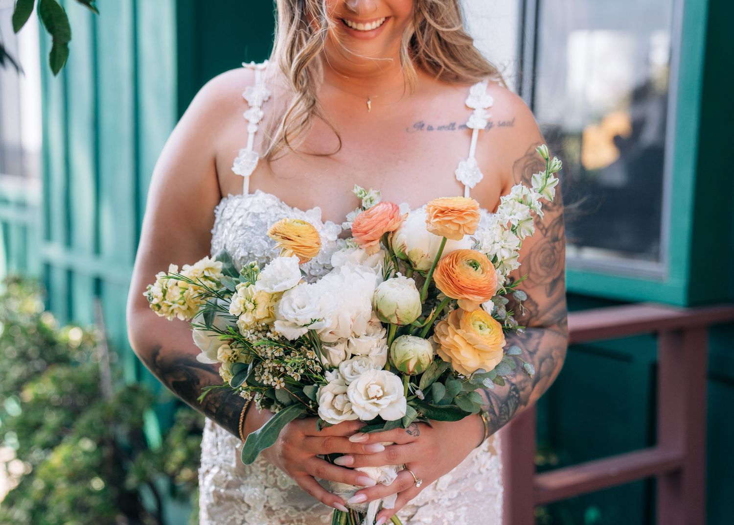 Elegant bridal bouquet featuring white and peach garden roses with delicate greenery against a teal backdrop.