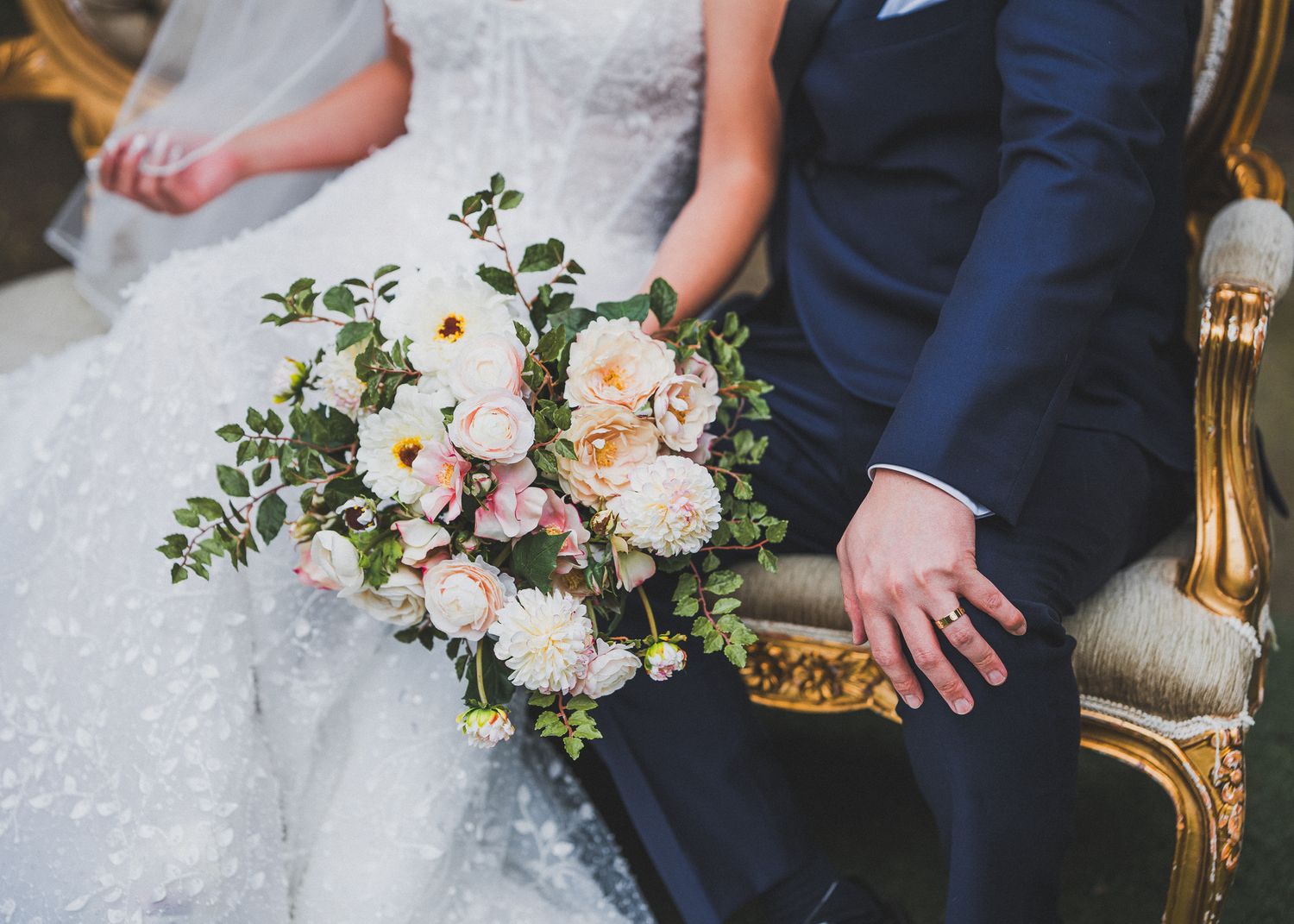 Wedding detail shots showing bridal bouquet with white and pink flowers next to dress fabric.
