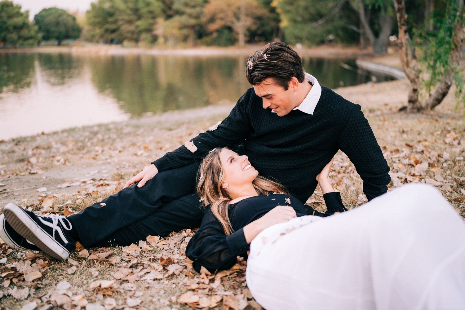 A couple shares tender moments by a waterfront during an engagement photoshoot.
