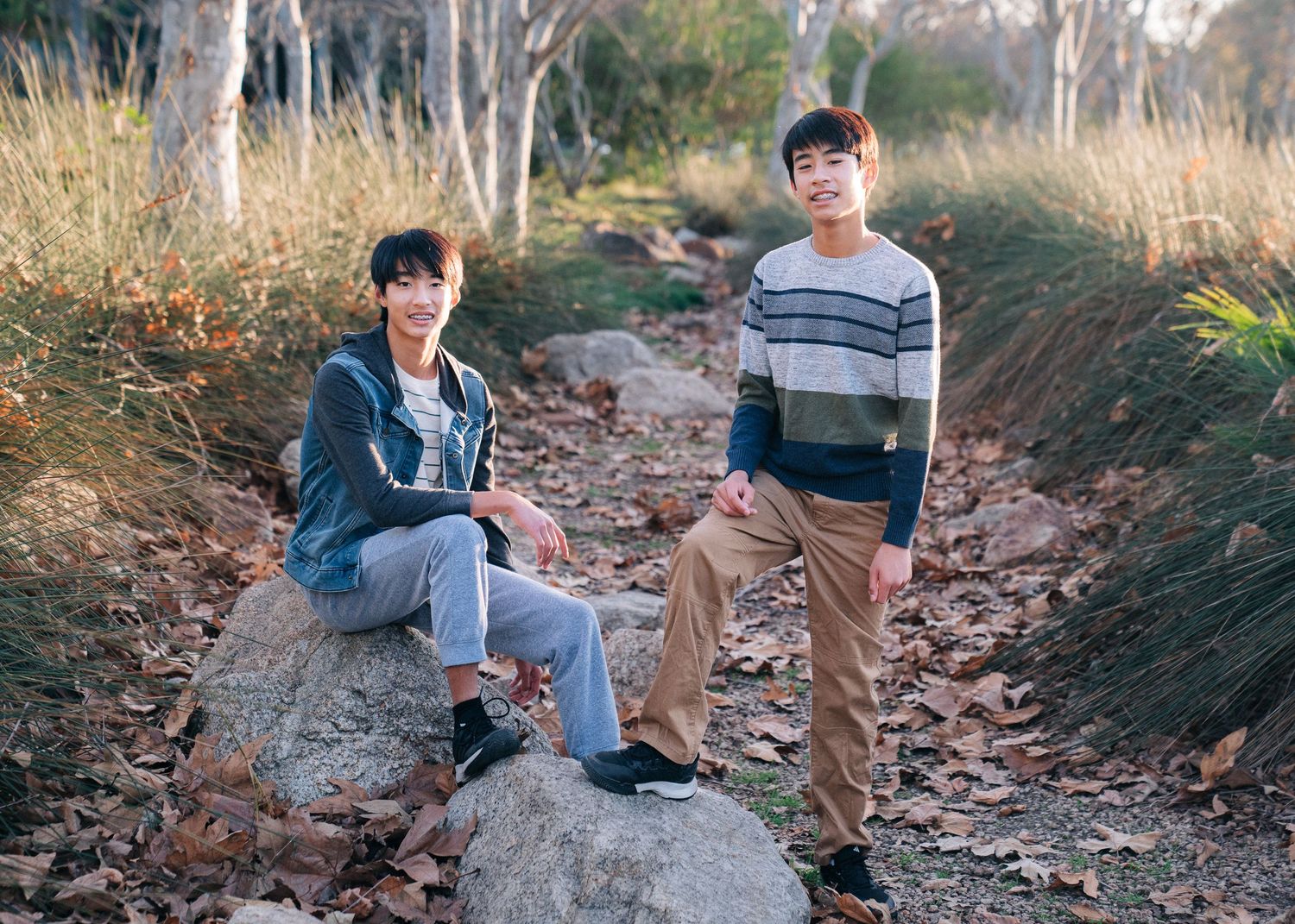 Two people relax on a rocky outcrop along a nature trail surrounded by autumn leaves.