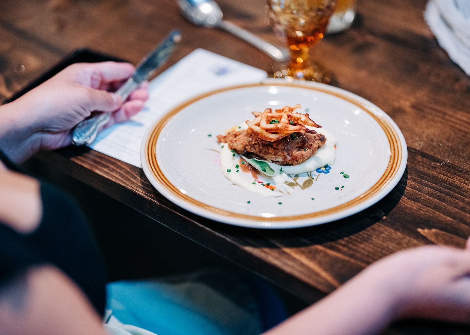 A plate with dessert garnished with crispy toppings sits on a rustic wooden table with amber glassware.