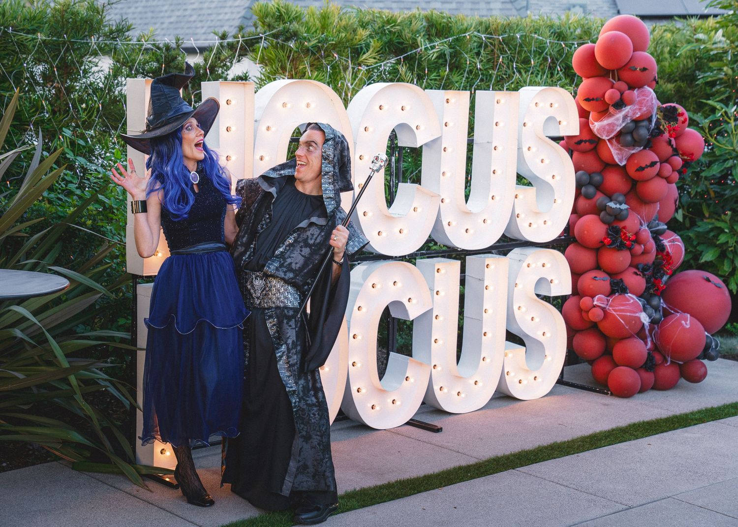 Large 'Hocus Pocus' light-up sign display decorated with red balloons against garden backdrop.