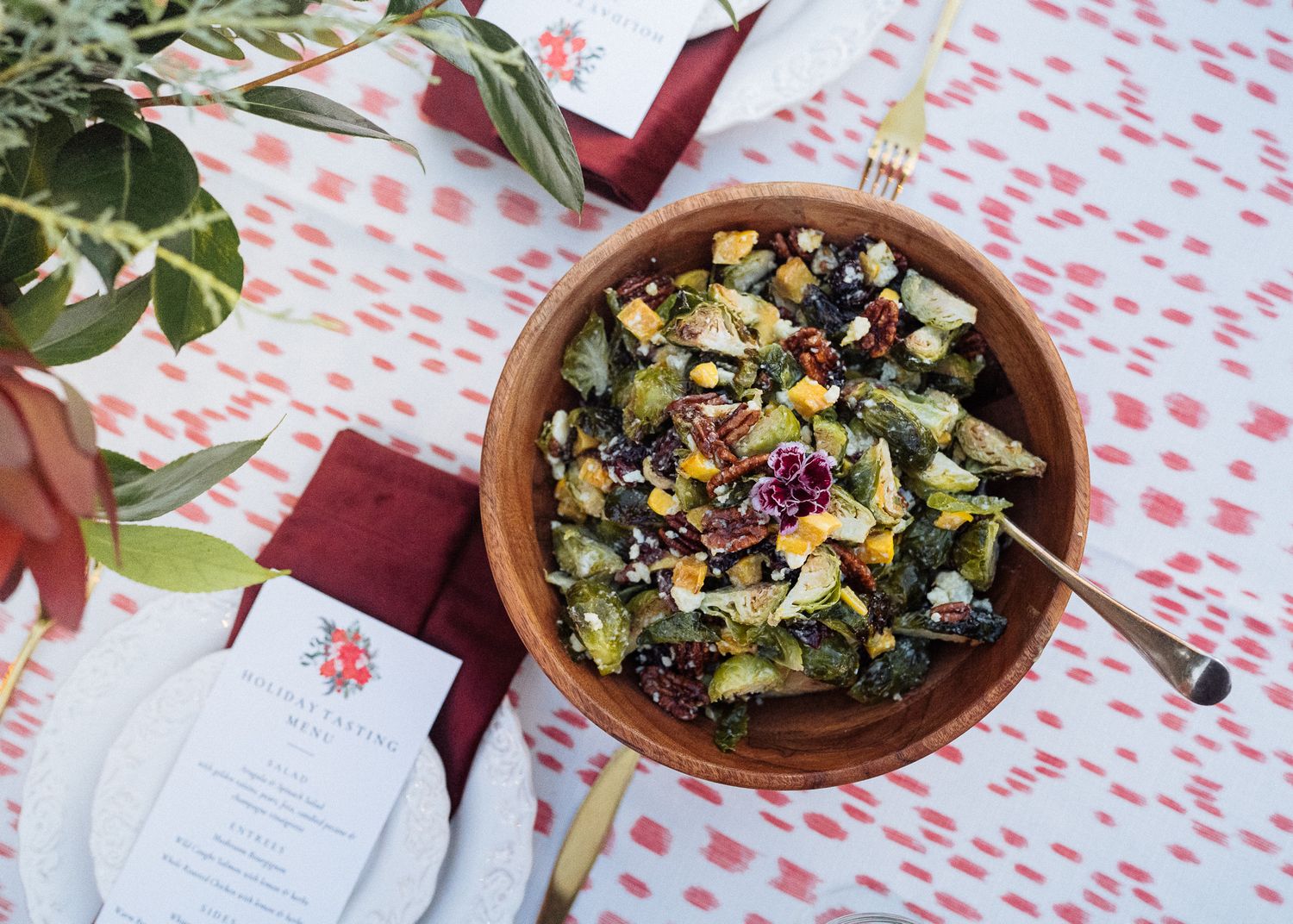 Colorful harvest salad with cranberries and nuts served in a wooden bowl on a polka dot tablecloth.
