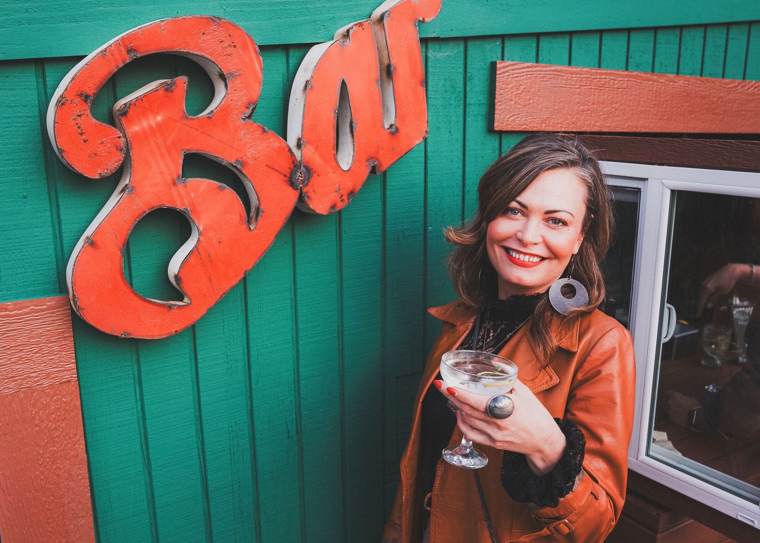 A cozy restaurant exterior with a large orange 'Bar' sign on green wooden siding.