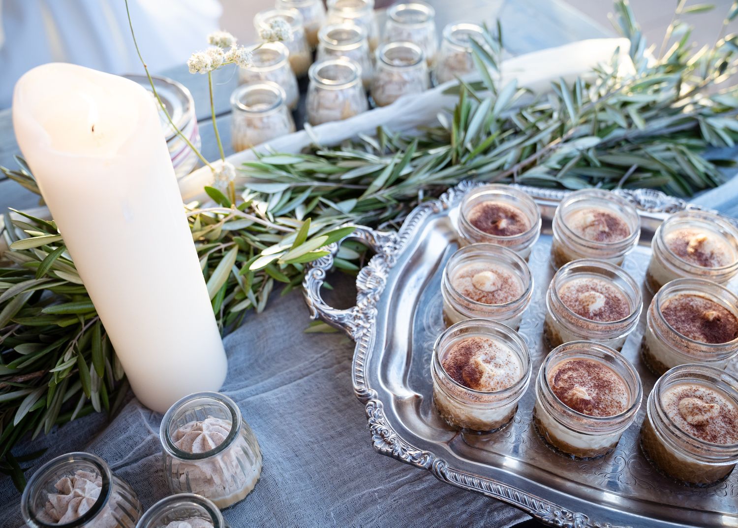 Small dessert mousse cups arranged on an elegant silver tray with fresh rosemary sprigs and a white candle.