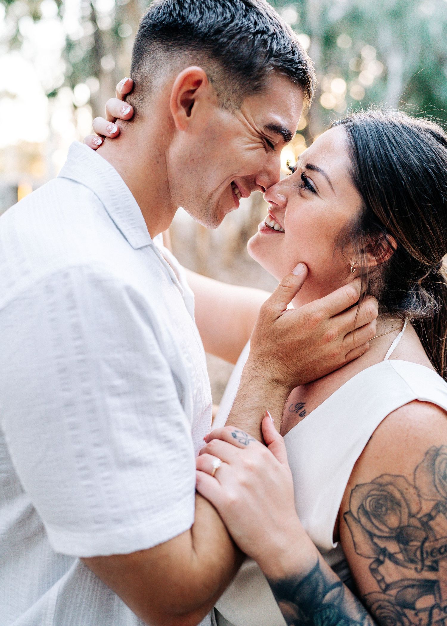 Intimate romantic couple embracing in white clothing outdoors with floral tattoo visible on one's arm.
