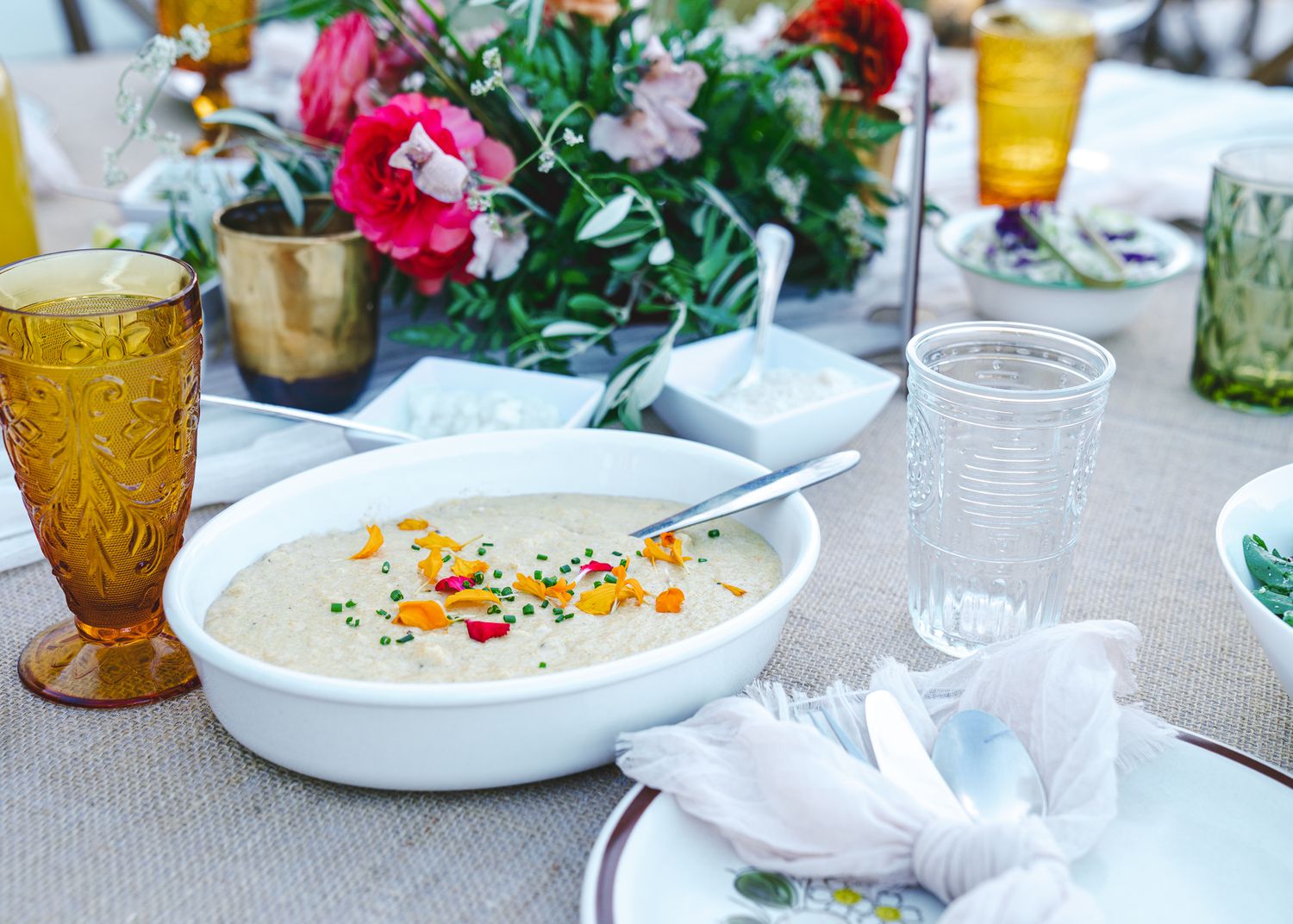 An elegant table setting with a creamy soup dish, amber glassware, and floral centerpiece.