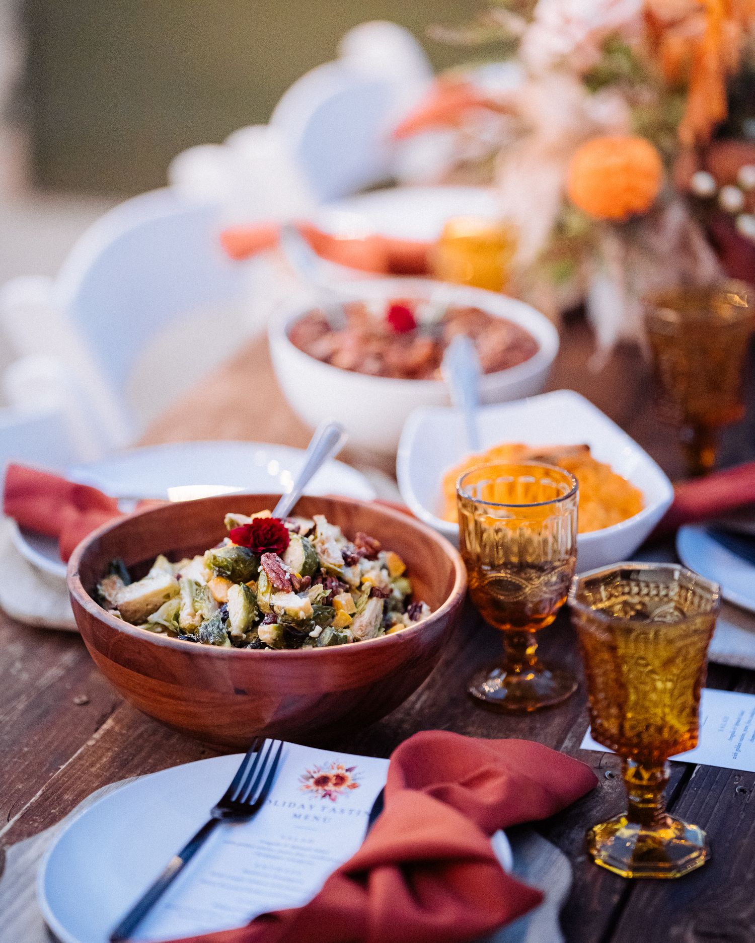 Rustic table setting with earthenware bowls, amber glasses and coral napkins for an elegant dinner party.