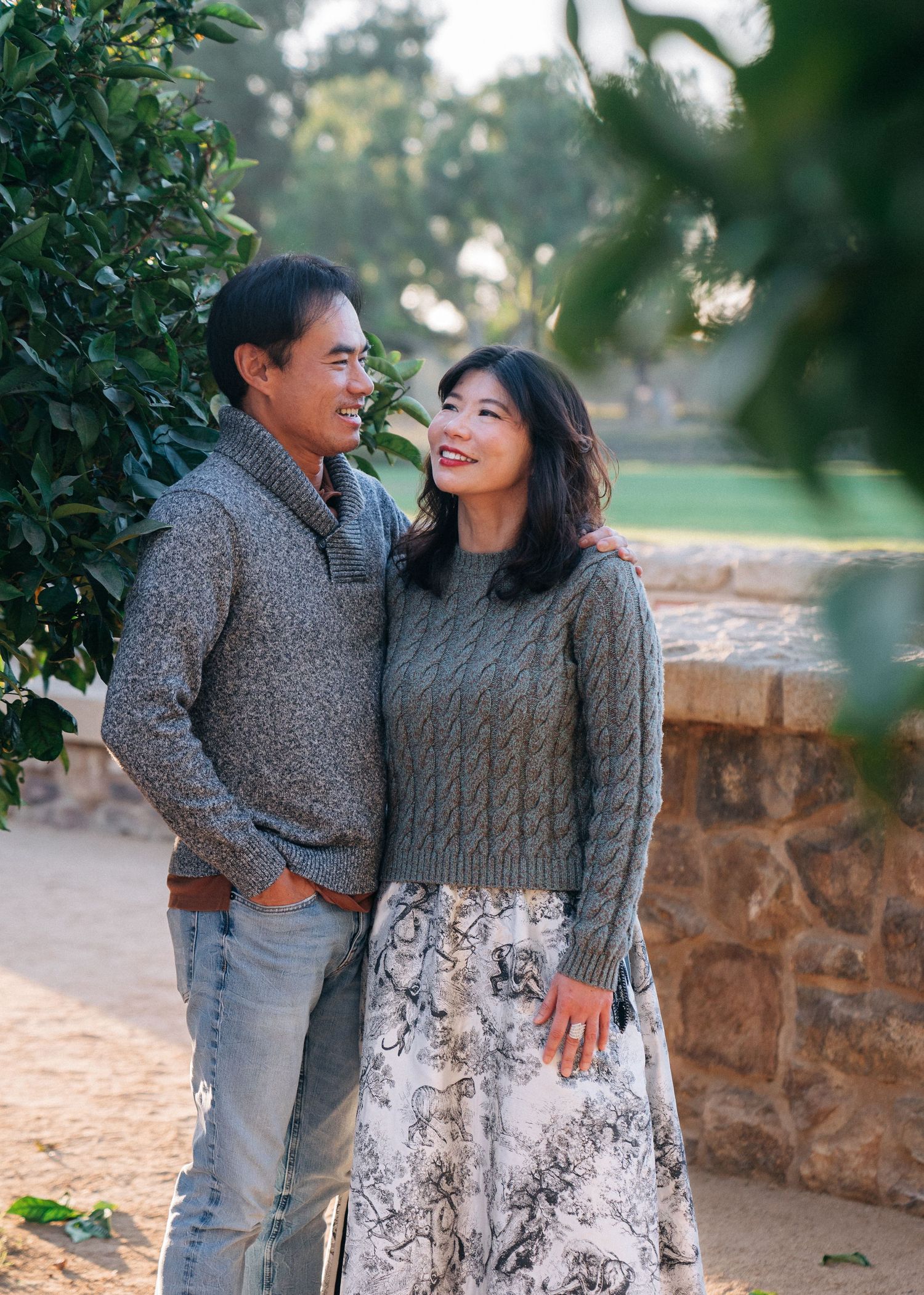 Two people in cozy cable knit sweaters share a tender moment together on a stone wall path during golden hour.