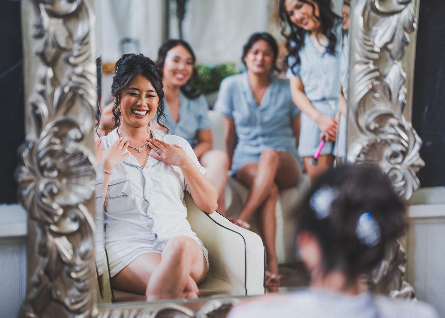Wedding party members share a candid moment while seated in an elegant room with ornate mirrors.