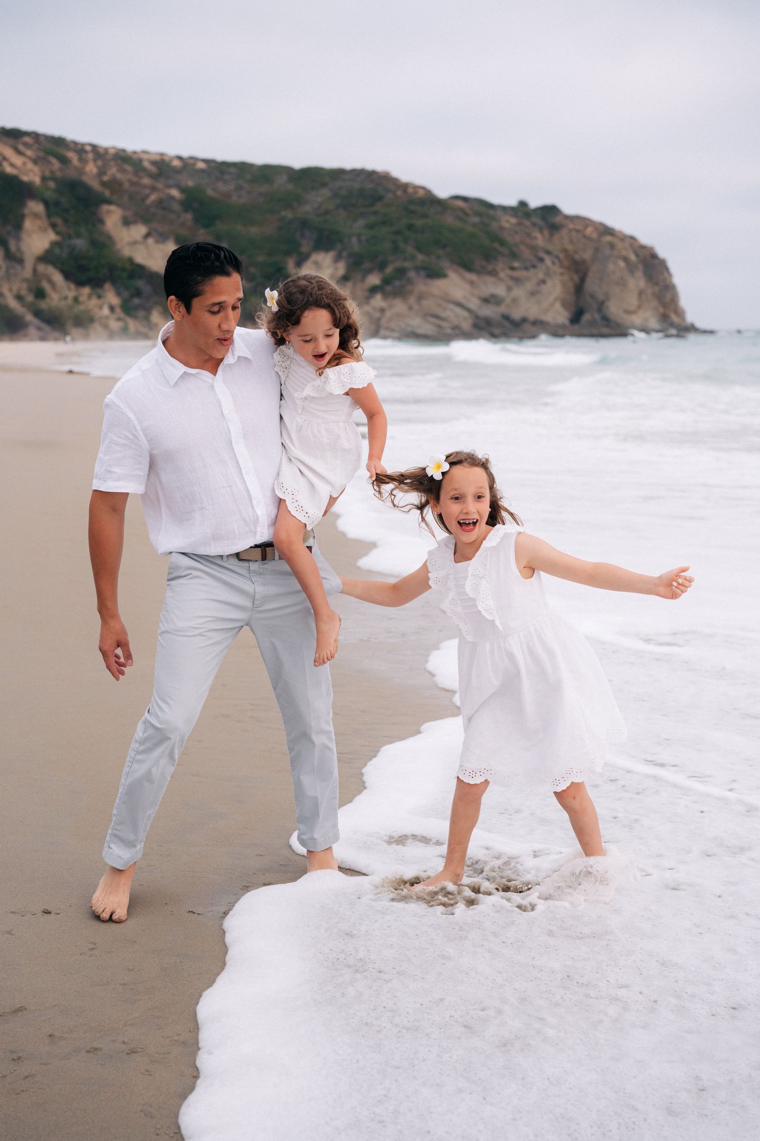 A couple enjoying playful moments at the beach with ocean waves and cliffs in the background.