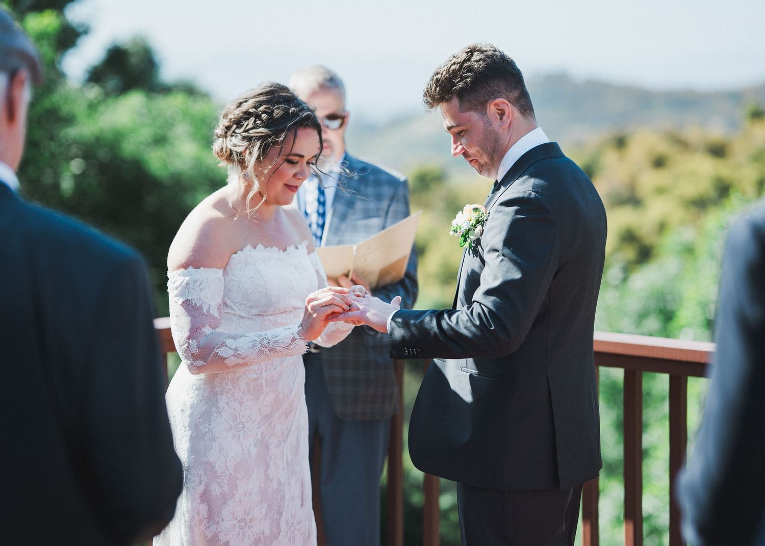 Wedding ceremony taking place on outdoor deck with couple exchanging rings.