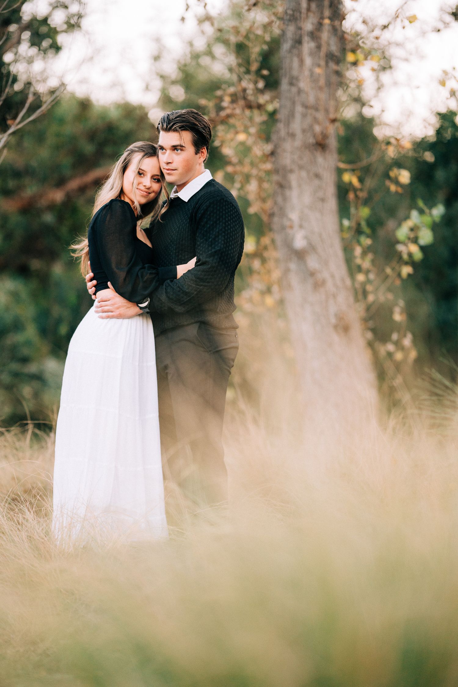 A romantic outdoor portrait showing a couple embracing in contrasting black and white outfits.