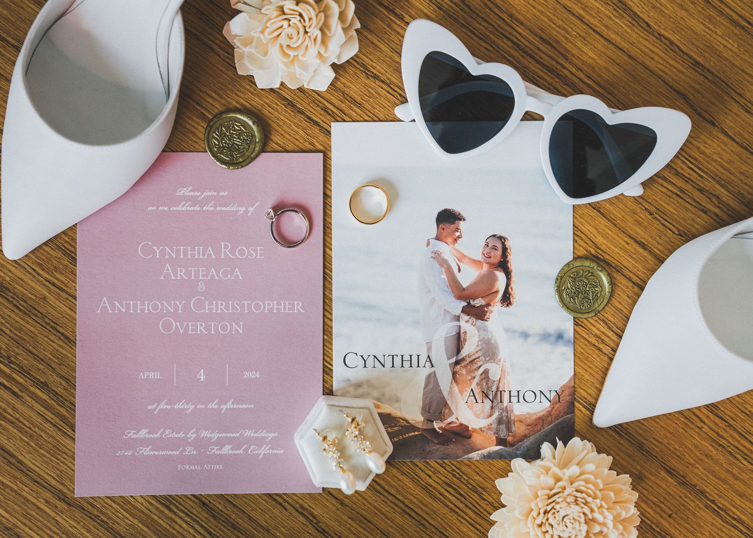 Wedding invitations and decorative elements laid out on a wooden surface with white and pink stationery details.
