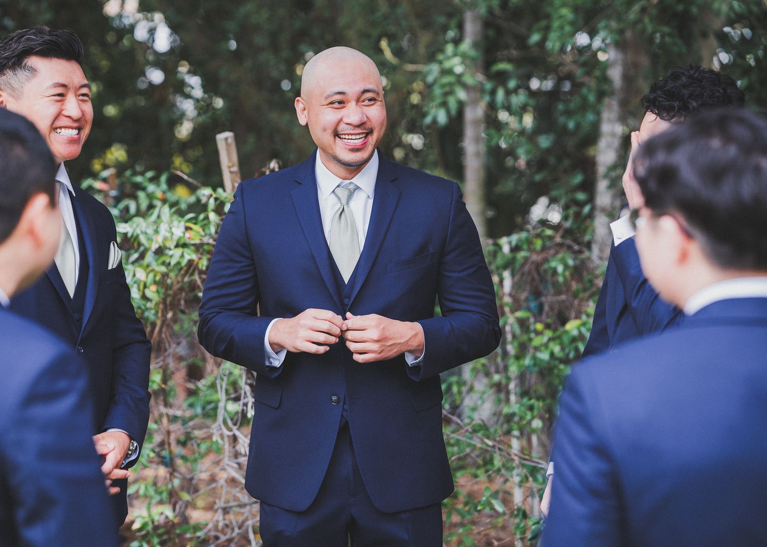 Wedding party in navy suits sharing candid moments in garden setting.