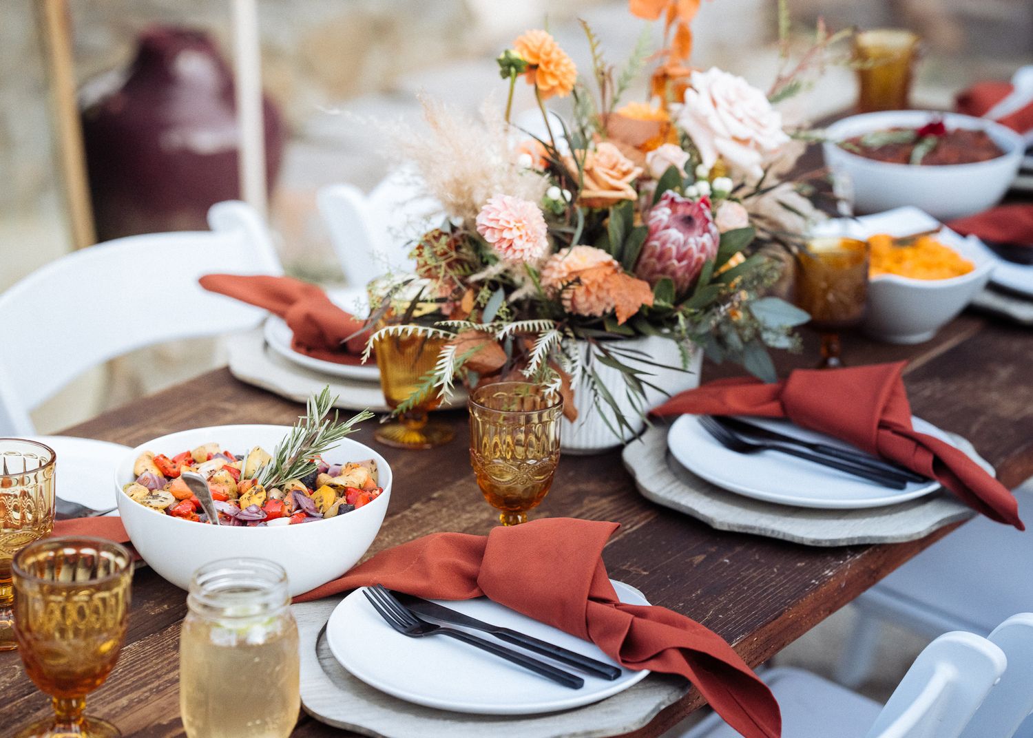Rustic tablescape with peach floral centerpiece, amber glassware, and burgundy napkins on wooden table.