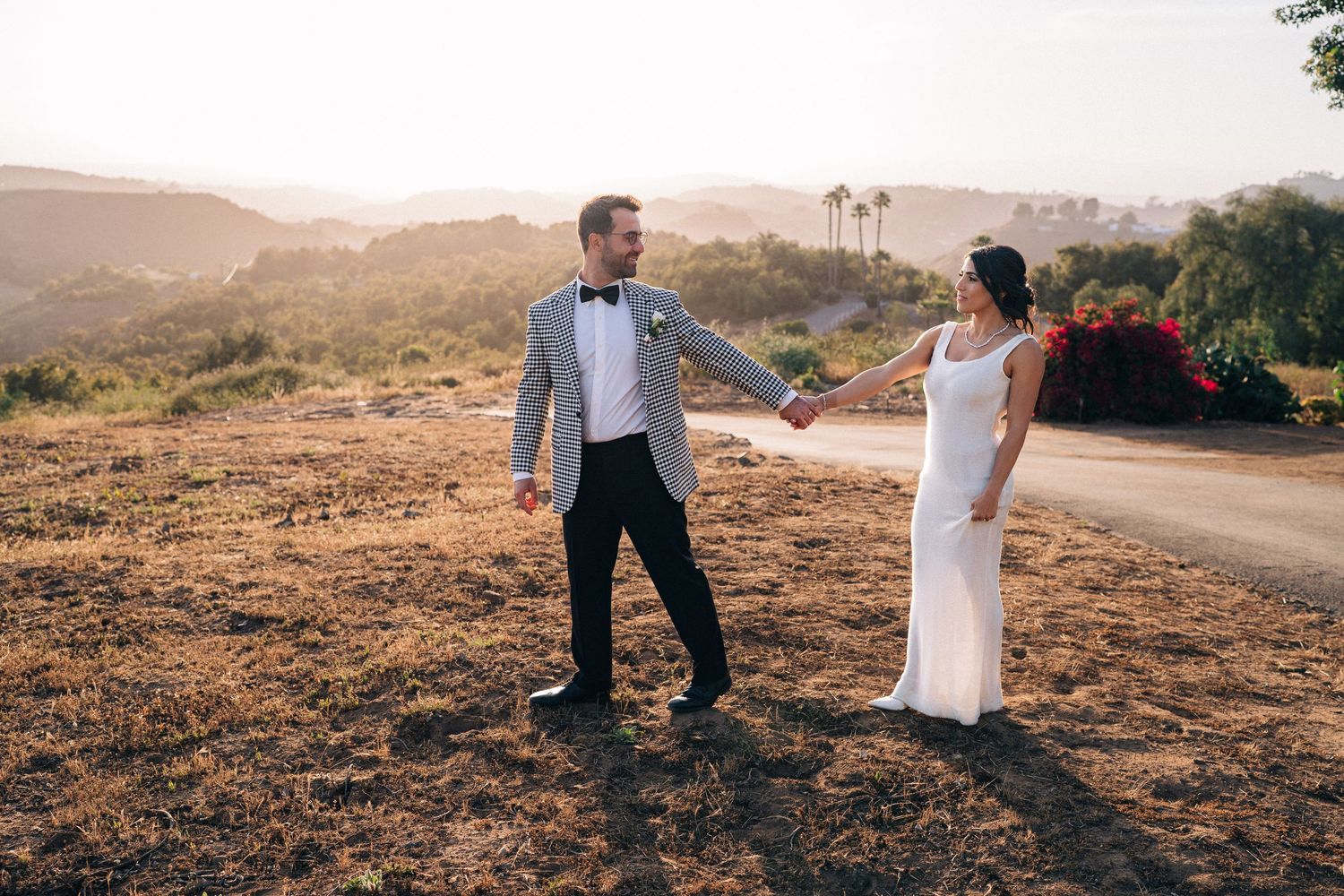 Newlyweds walking together on rustic hillside during sunset photo session.