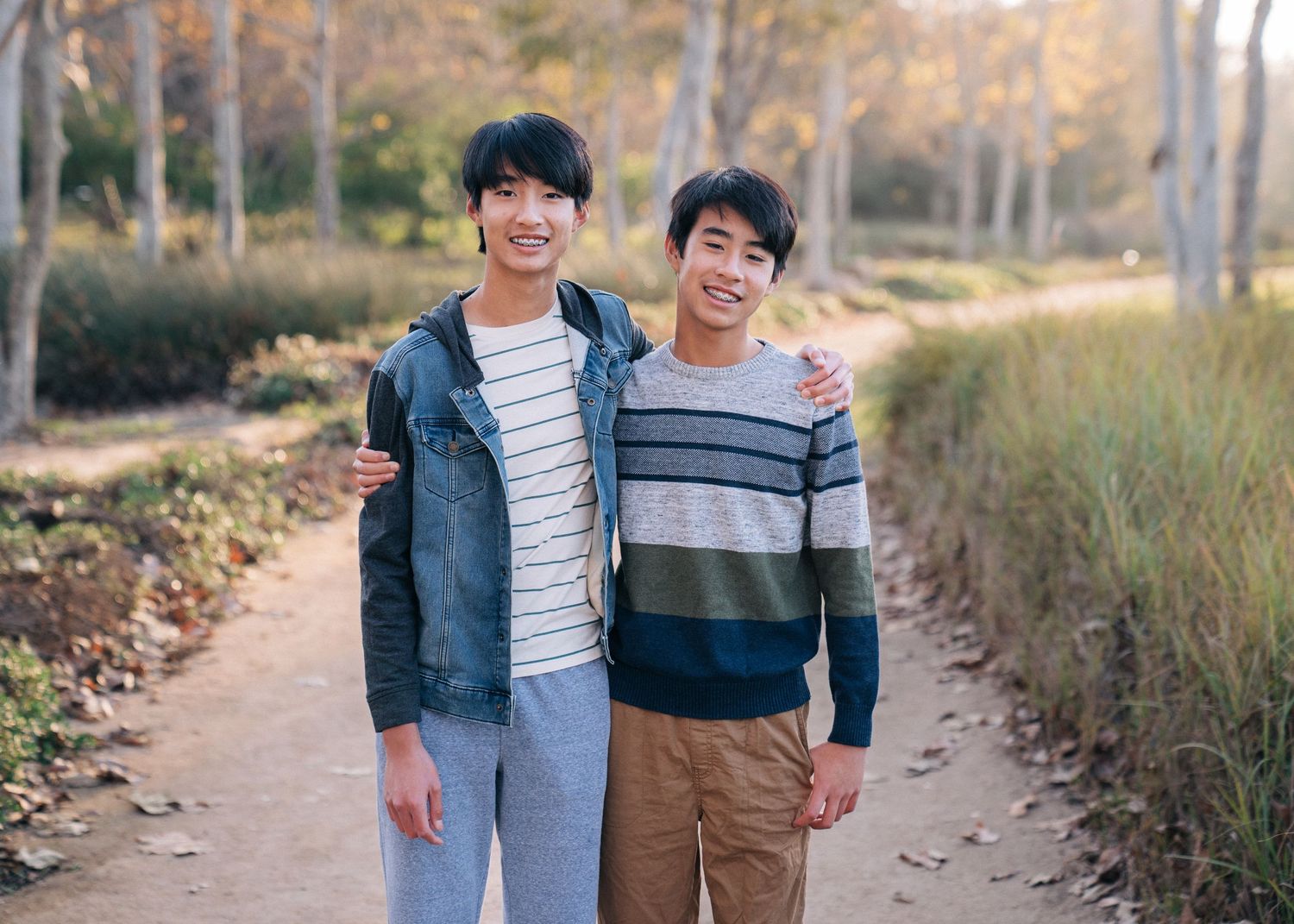 Two friends in casual sweaters share a friendly moment while walking on an autumn forest trail.