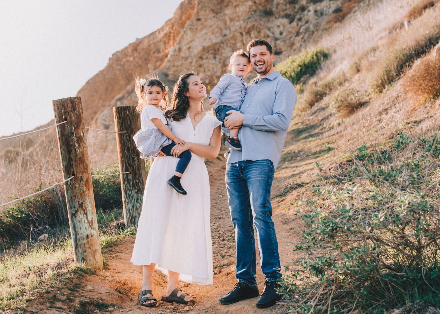 A family enjoys time together on a scenic hillside trail during golden hour as the sun sets behind them.