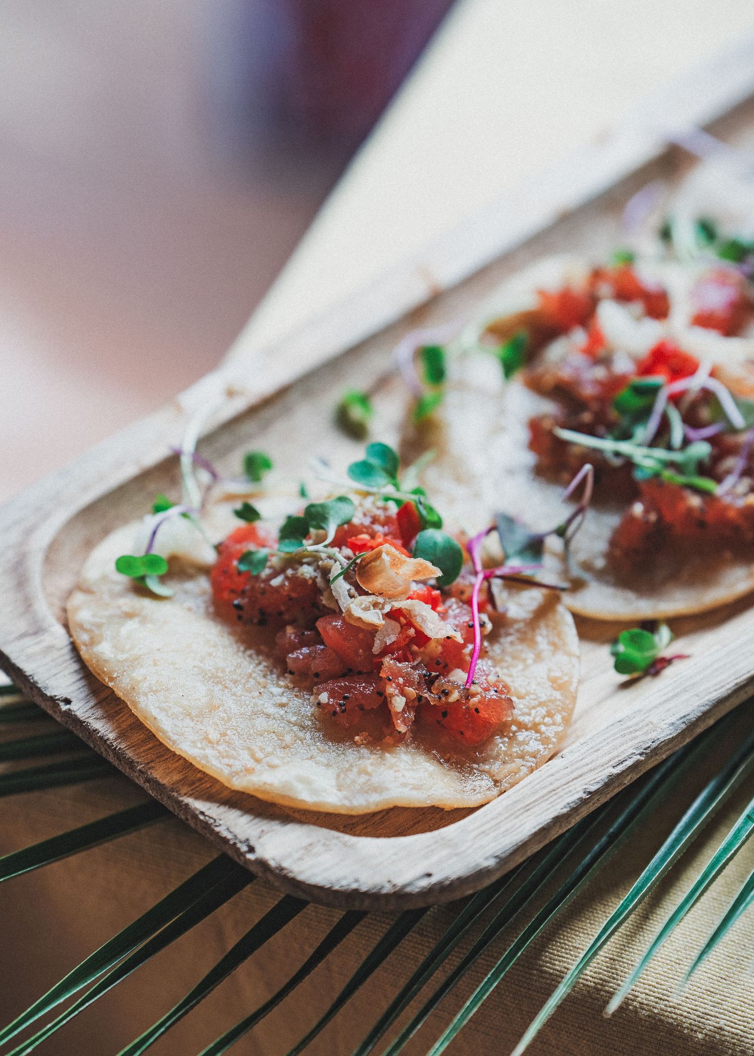 Fresh fish tacos topped with microgreens and pico de gallo served on corn tortillas on a wooden platter.