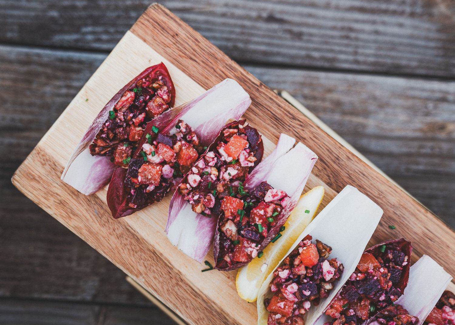 Fresh tacos with colorful hibiscus flower garnish served on a rustic wooden cutting board.