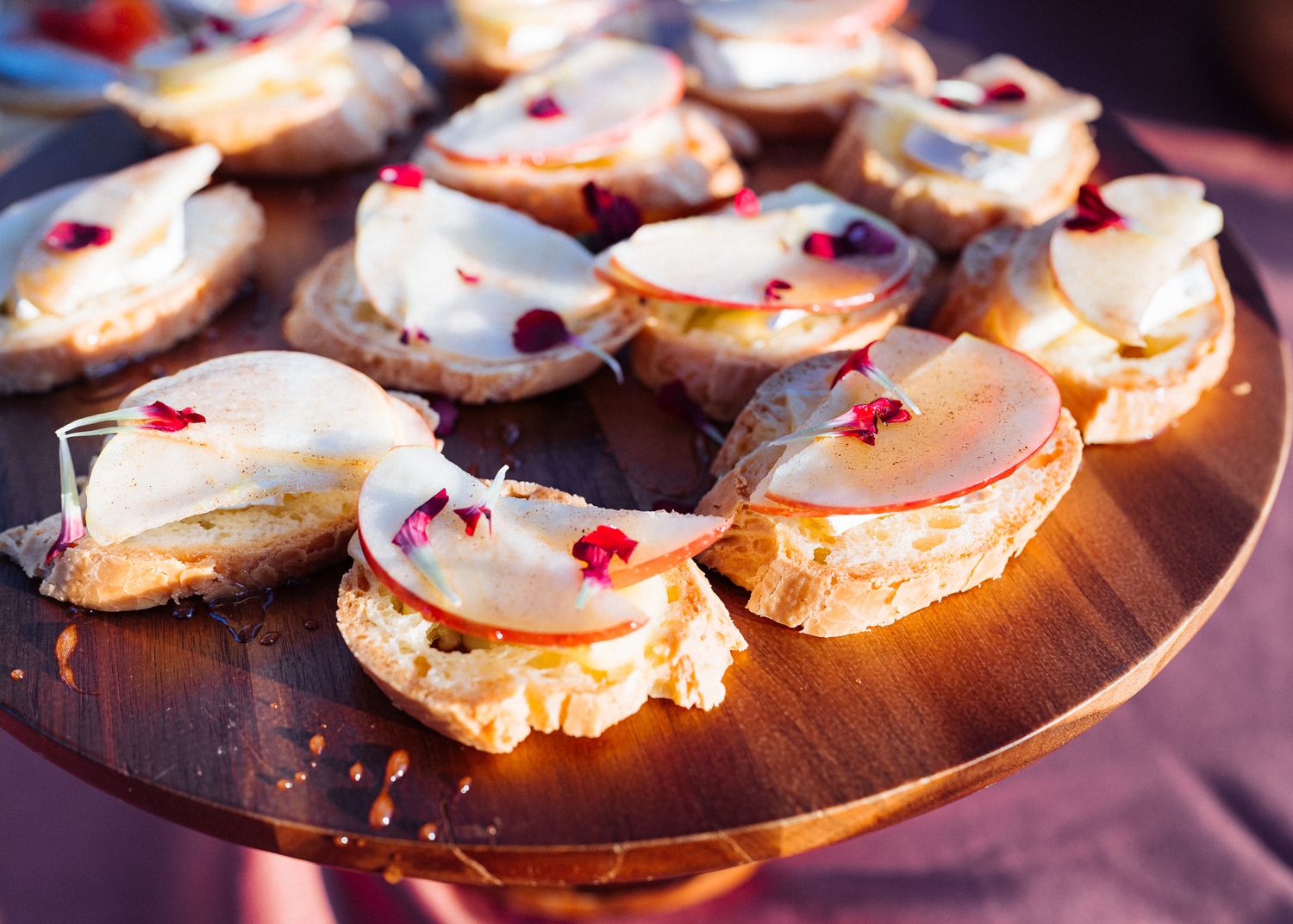 Artisanal canapes with sliced pears and garnishes arranged on a wooden serving platter.