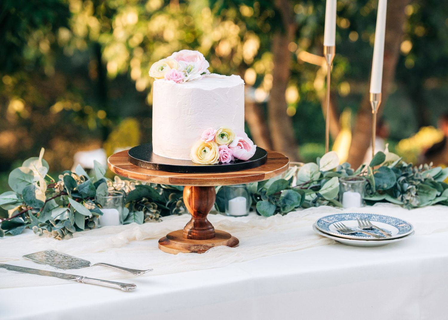 Wedding dessert table with eucalyptus garland and elegant copper cake stand on white tablecloth.