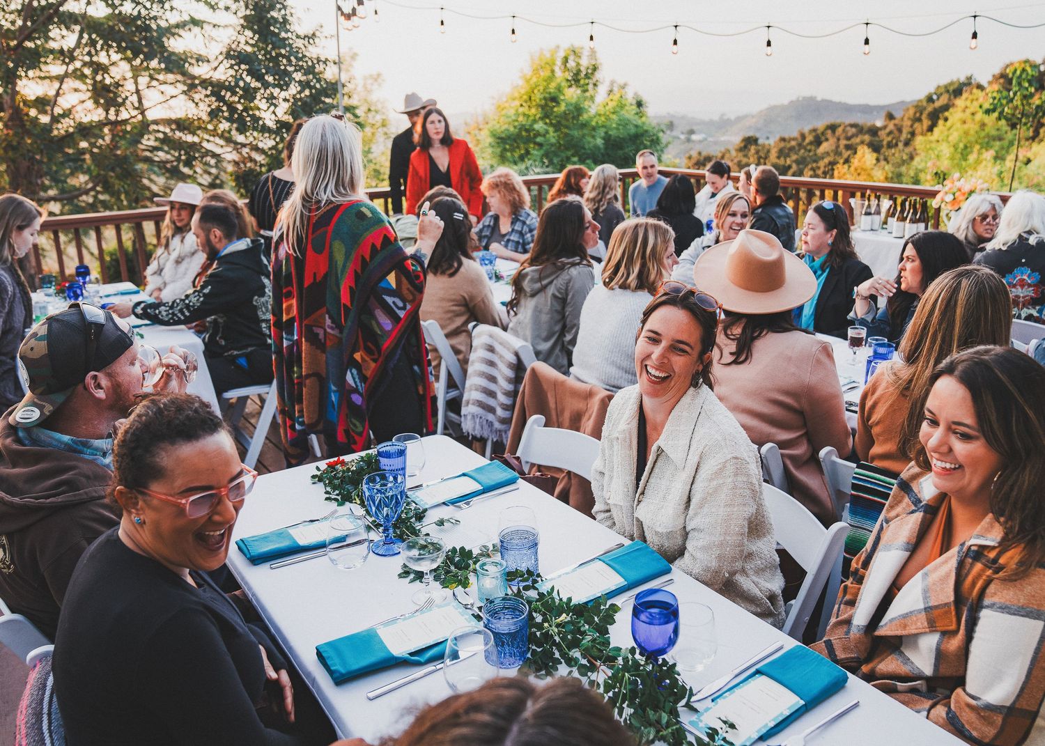 A large outdoor dinner party with guests seated at decorated tables during golden hour.