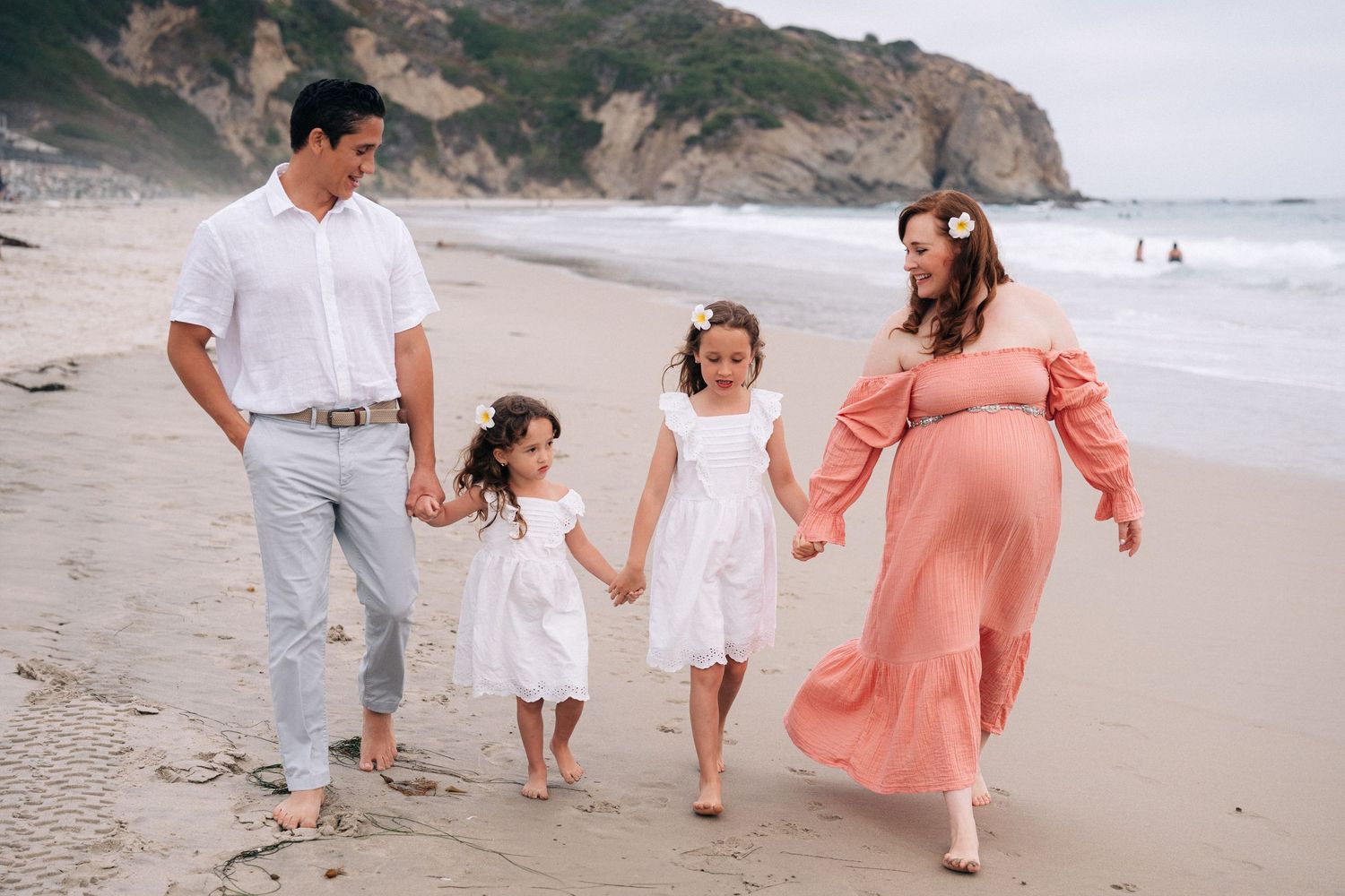Family walking and playing together along a coastal beach with cliffs in the background.