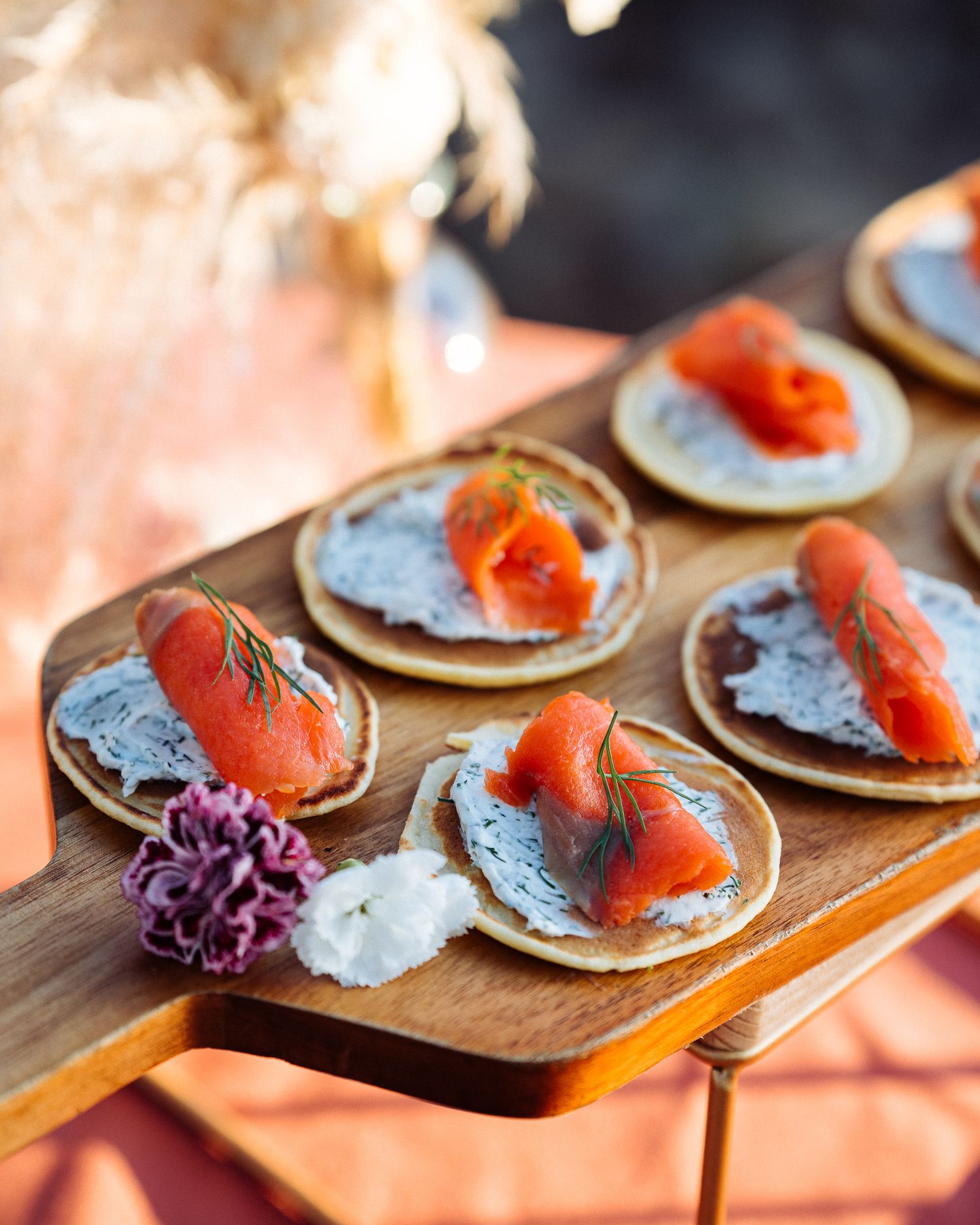 Smoked salmon blinis topped with creme fraiche and garnished with fresh dill on a wooden serving board.