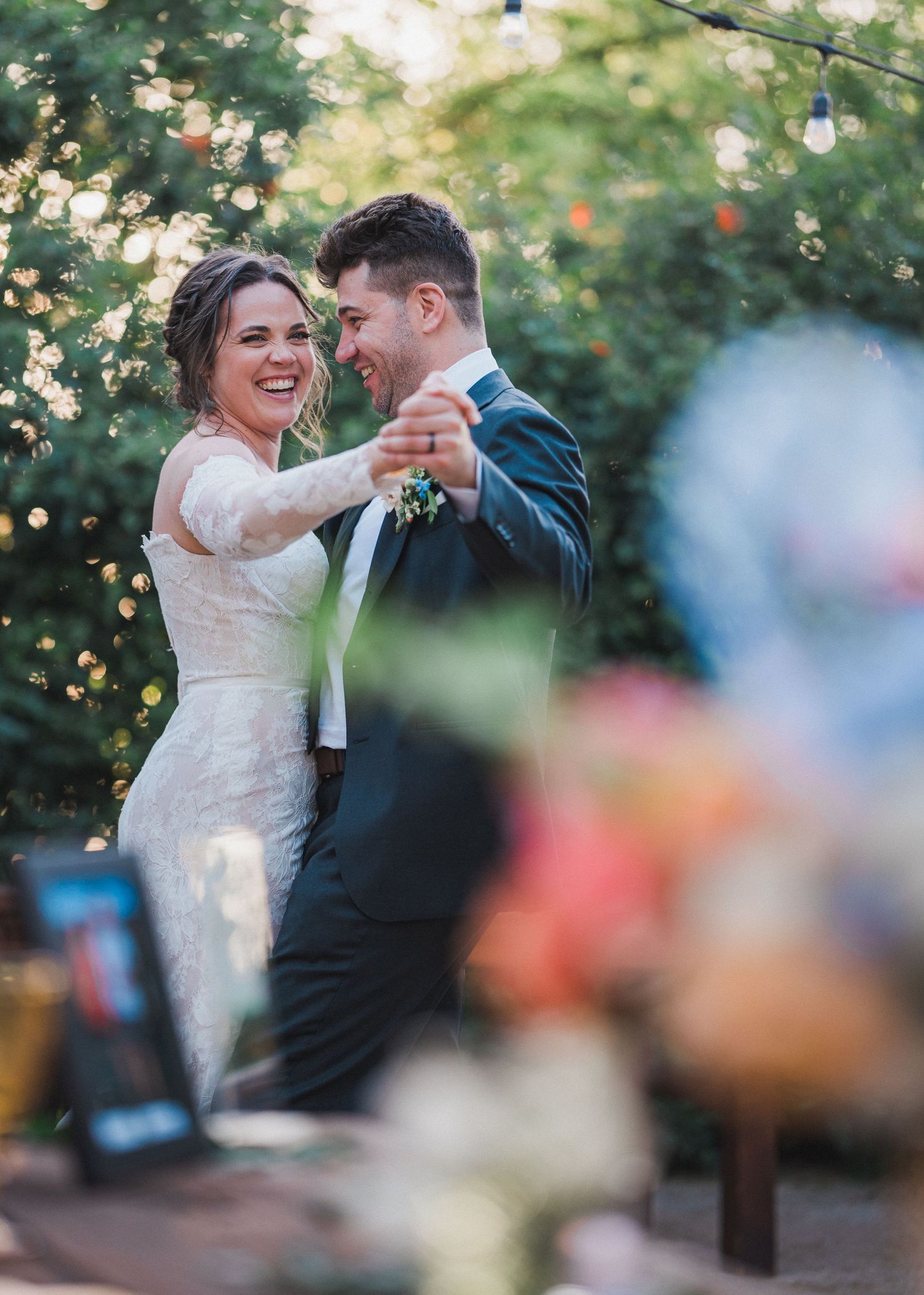 Joyful couple share their first dance under twinkling outdoor lights at sunset wedding reception.