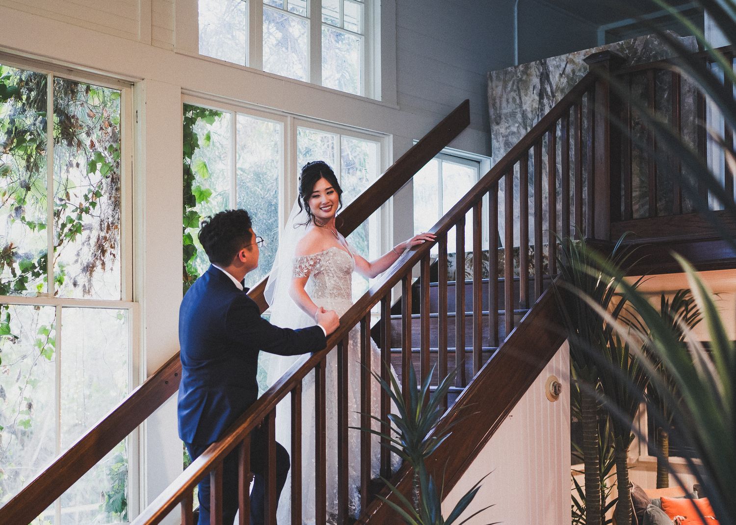 A couple shares a romantic moment on an elegant wooden staircase in a sunlit indoor setting.