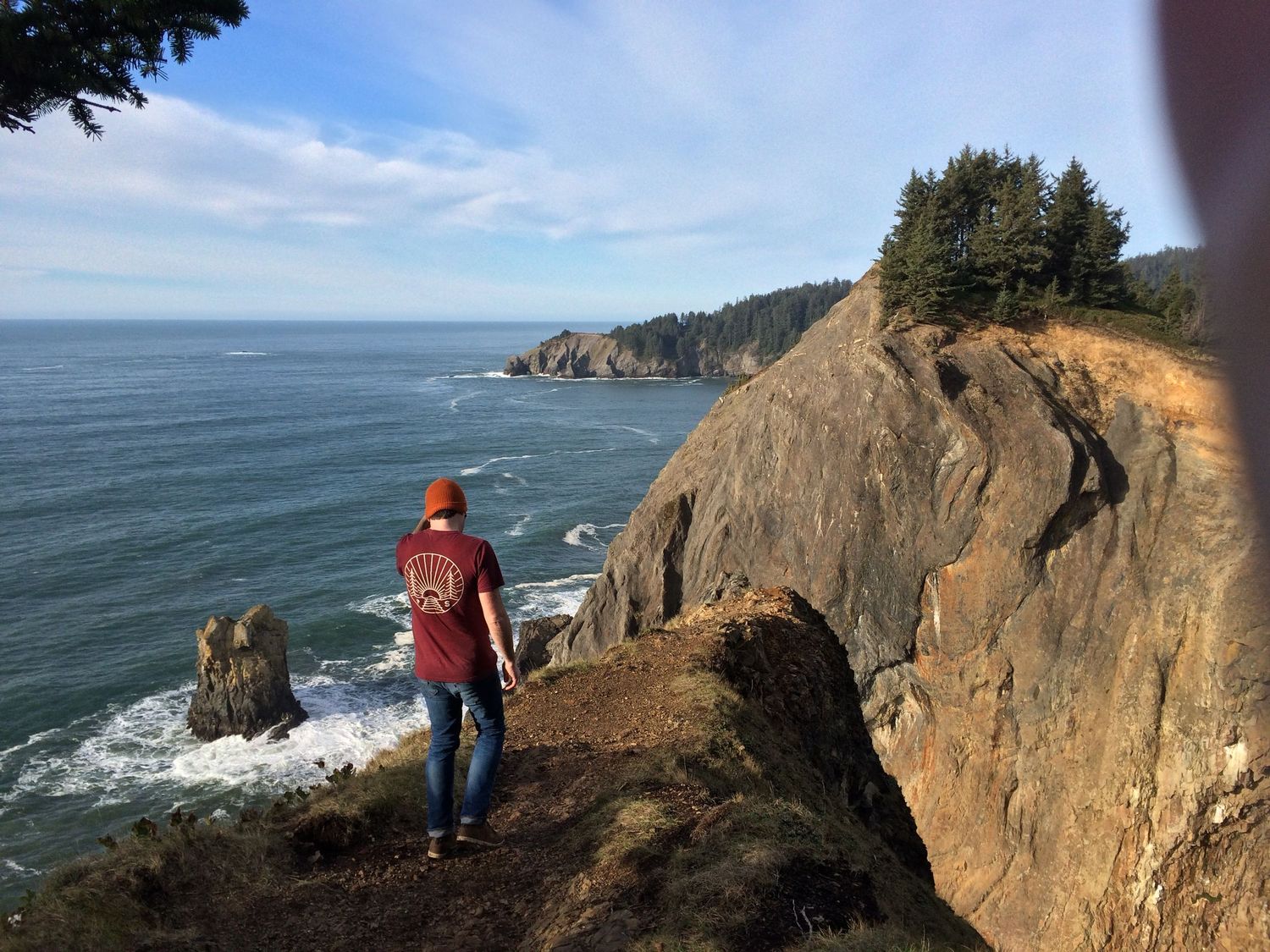 Hikers explore rugged coastal cliffs overlooking the Pacific Ocean on a sunny day at an Oregon viewpoint.