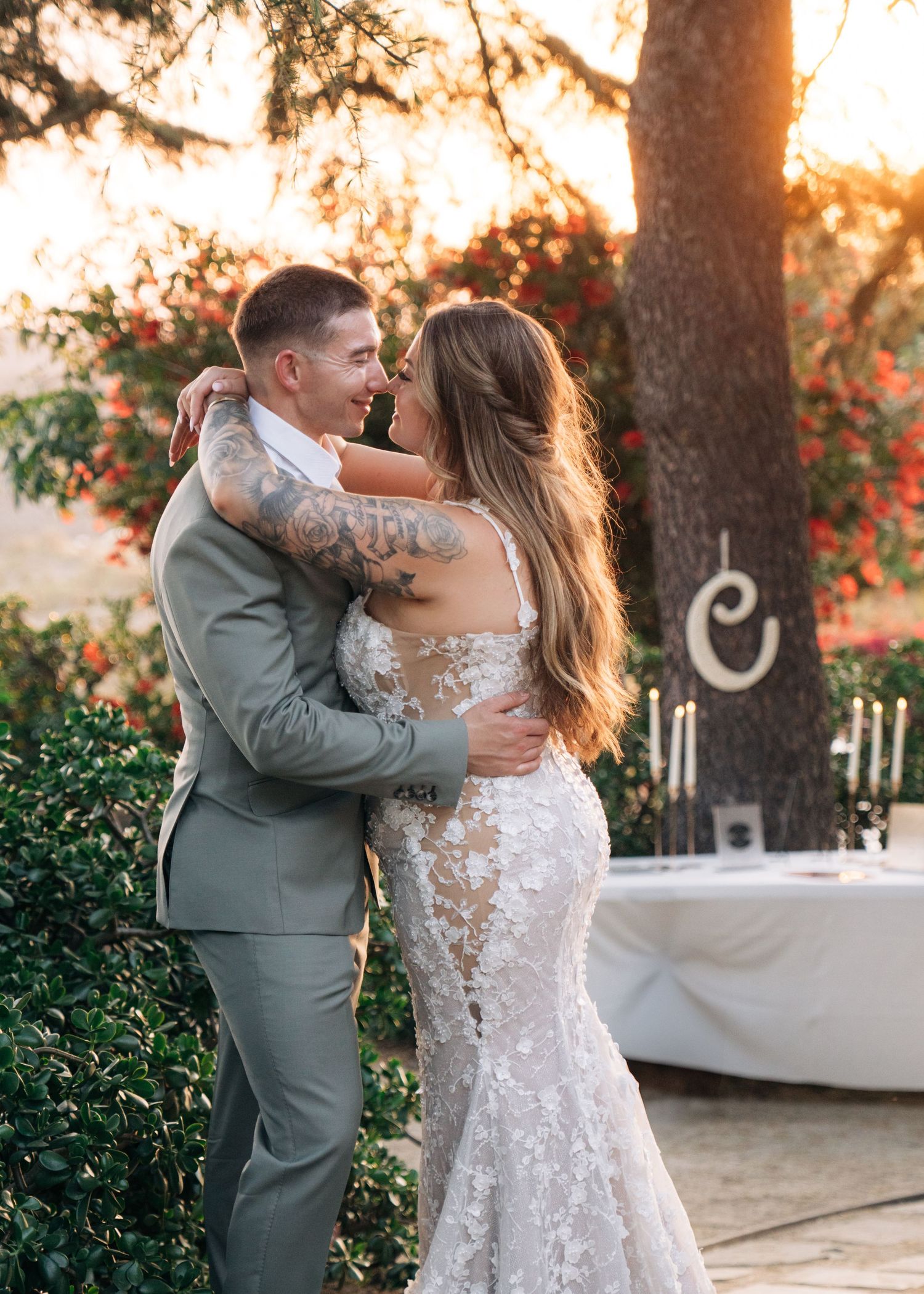 A couple shares an intimate moment at sunset during their wedding, with romantic lighting and floral decor in the background.