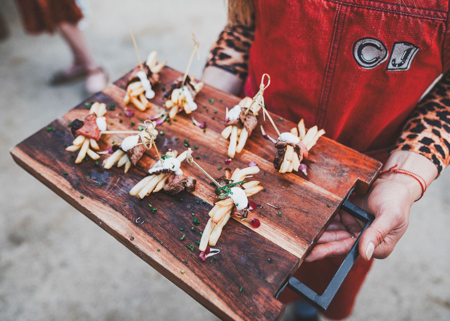 Small decorative corn husk dolls arranged on a rustic wooden board with someone in a red apron.