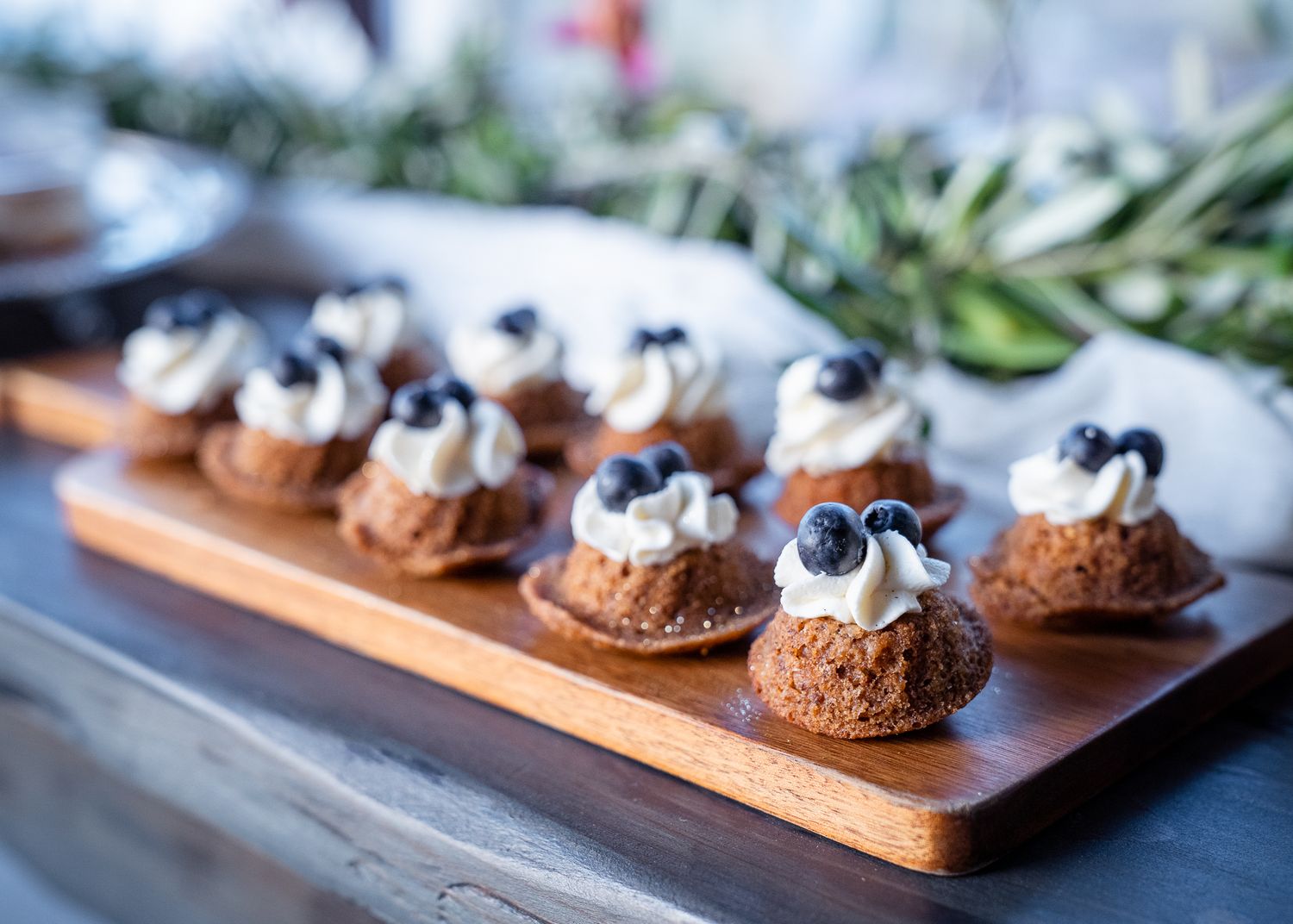Mini chocolate pastries topped with whipped cream and fresh blueberries arranged on a wooden serving board.