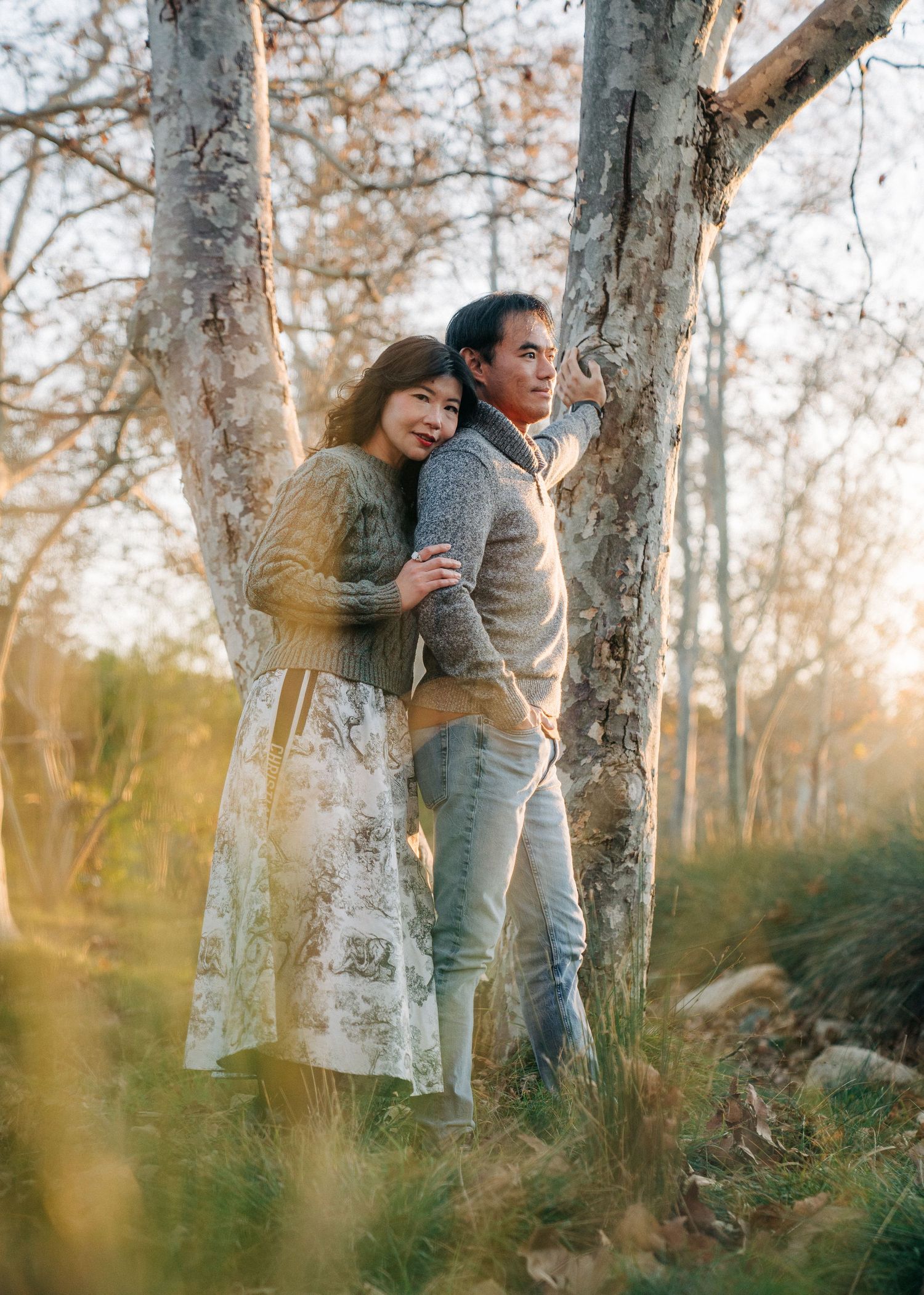 A couple hugs and smiles together among trees at sunset, creating a romantic autumn atmosphere in nature.