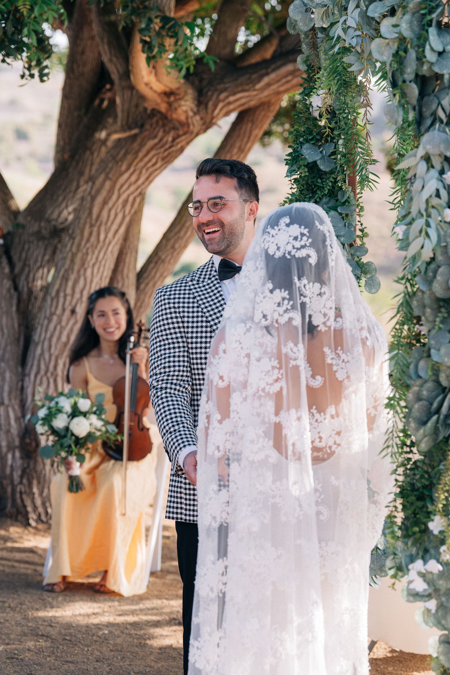 A joyful wedding ceremony moment under a tree decorated with hanging greenery and florals.