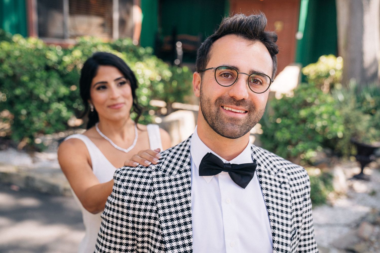 Wedding couple in black and white checkered attire pose for romantic photos in an outdoor garden setting.