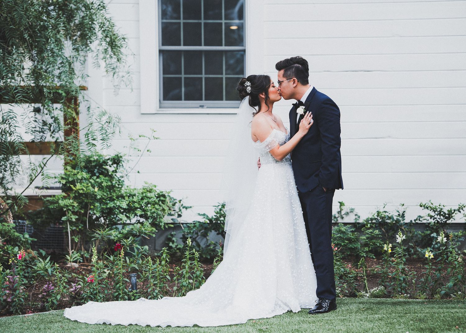 Romantic wedding couple portraits in front of a white building with classic framed windows and garden landscaping.