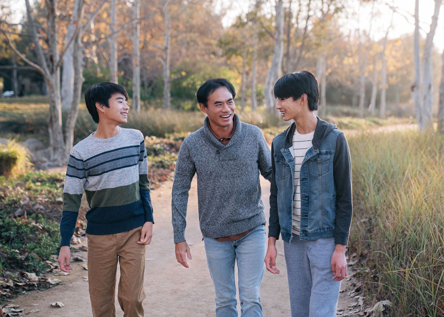 Three companions walk together and chat on a scenic dirt path surrounded by fall foliage.