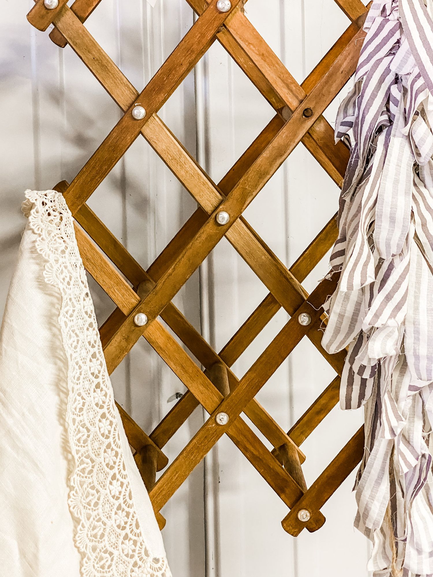 Wooden accordion-style wall mounted rack with lace and textile items hanging.
