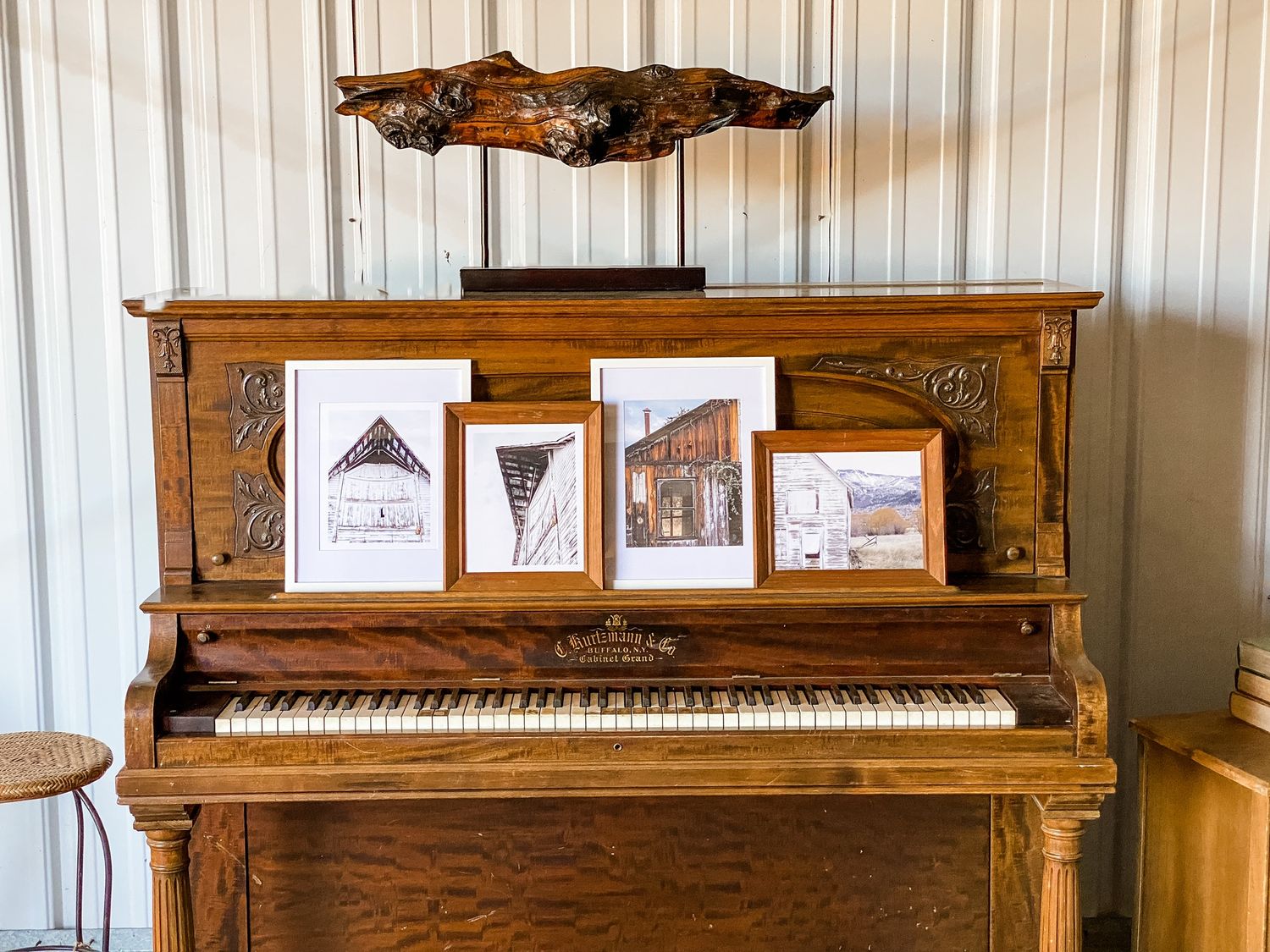Vintage upright piano with framed artwork displayed on top against white beadboard wall.