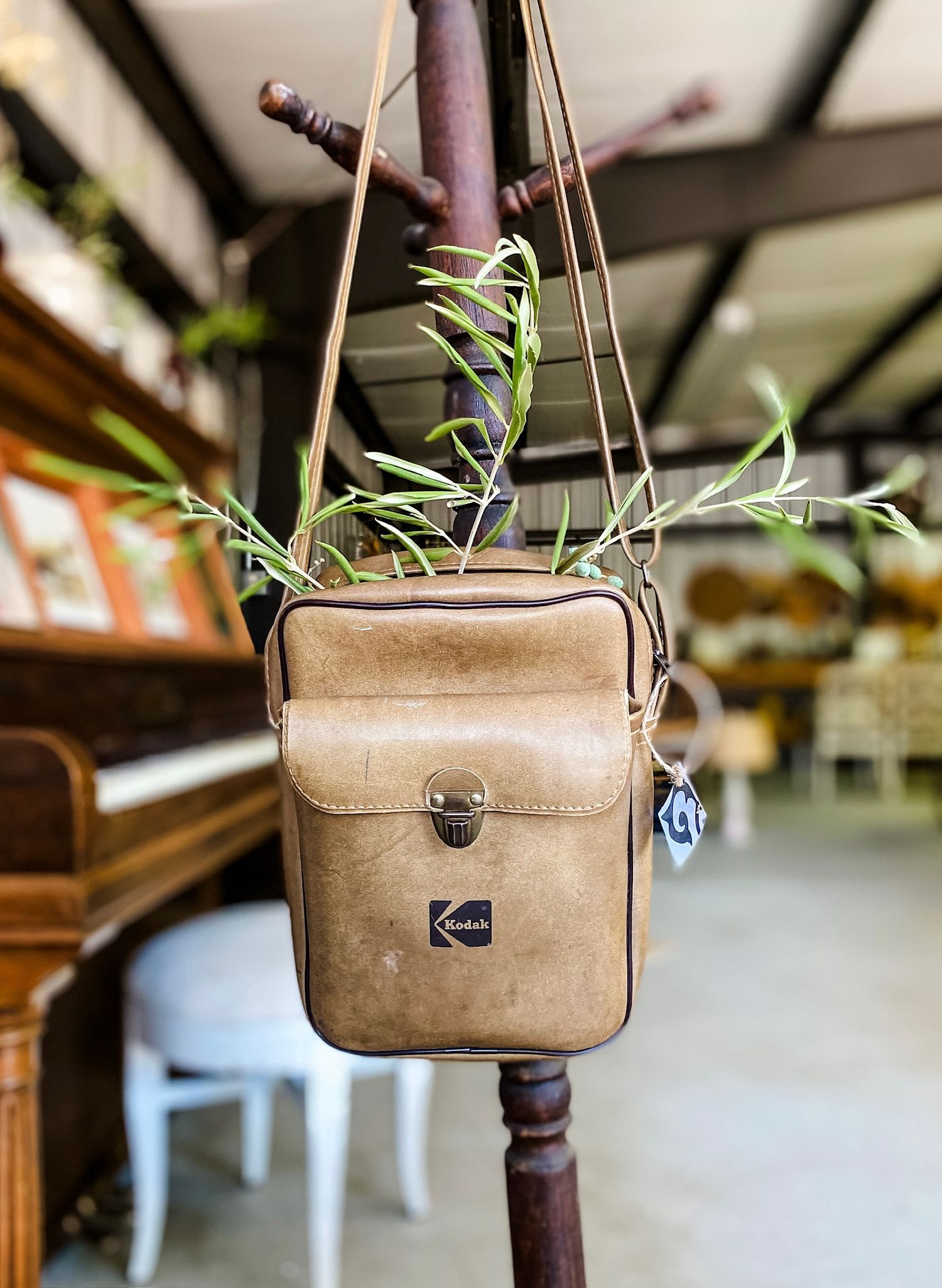 Vintage tan leather Kodak camera bag hanging on a wooden stand.