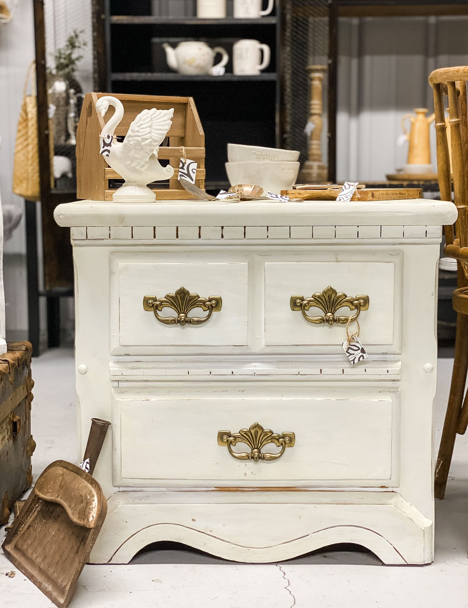 Vintage white painted nightstand with ornate brass handles and decorative white ceramic teapot on top.