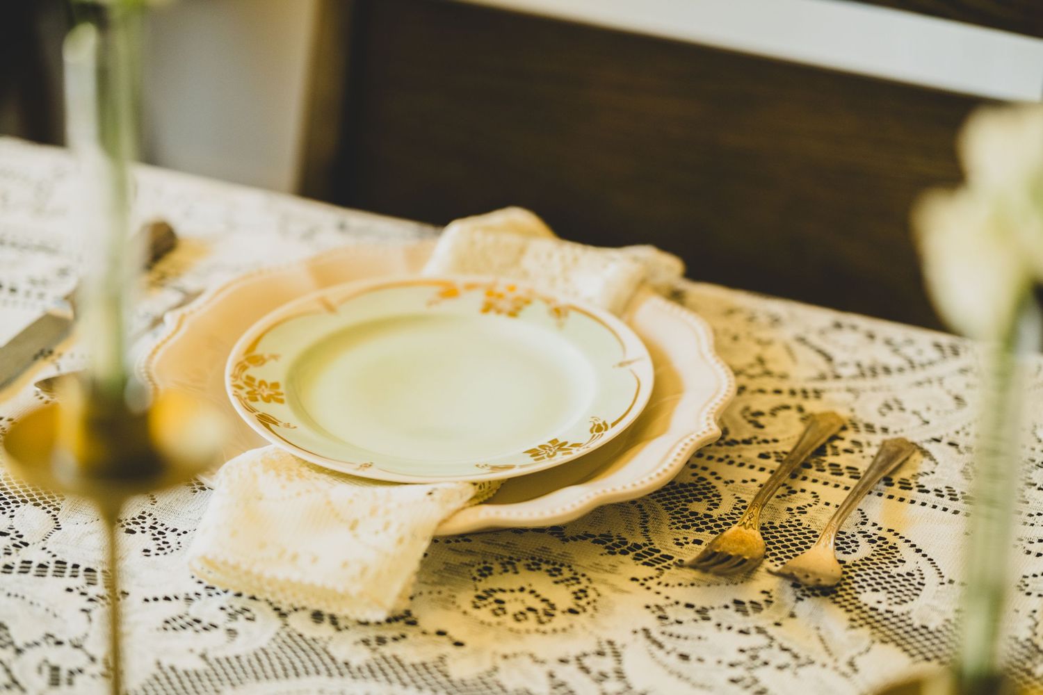 Elegant vintage place setting with gold-rimmed plates, lace napkin, and gold cutlery on a white lace tablecloth.
